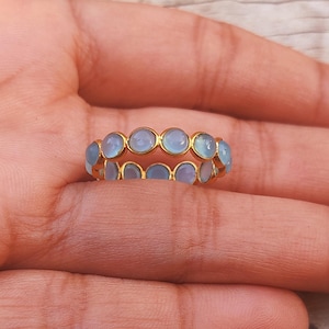 May include: A gold ring with a double row of light blue gemstones. The ring is on a person's finger.