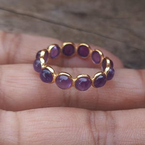 Op de afbeelding: Een gouden ring met een band van paarse edelstenen. De ring is gemaakt van metaal en heeft een eenvoudig ontwerp.