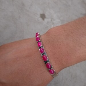 May include: A silver bracelet with pink oval-shaped stones. The bracelet is on a person's wrist.