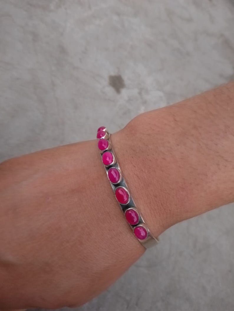 May include: A silver bracelet with pink oval-shaped stones. The bracelet is on a person's wrist.