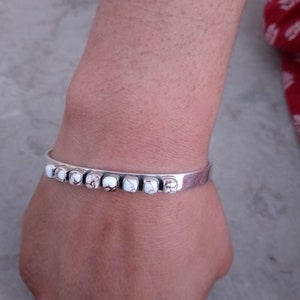 May include: A silver bracelet with white and brown stones. The bracelet is on a person's wrist.