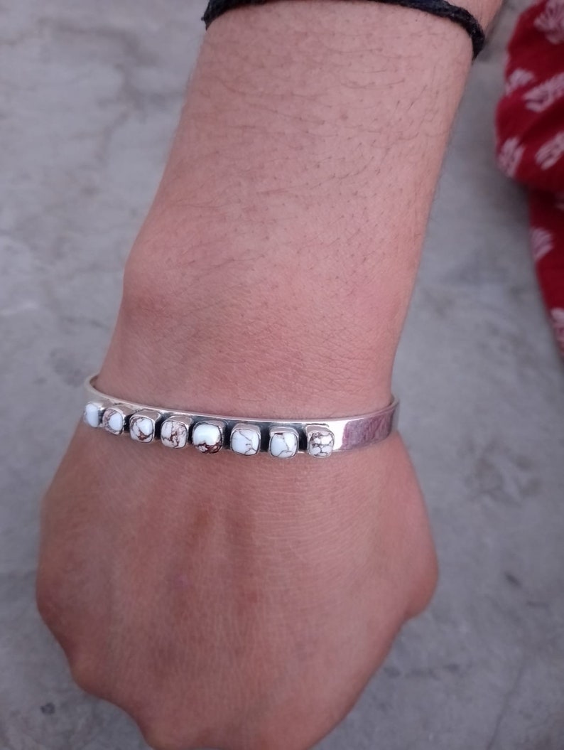 May include: A silver bracelet with white and brown stones. The bracelet is on a person's wrist.
