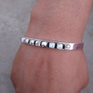 May include: A silver bracelet with white and brown stones. The bracelet is open and has a simple design.