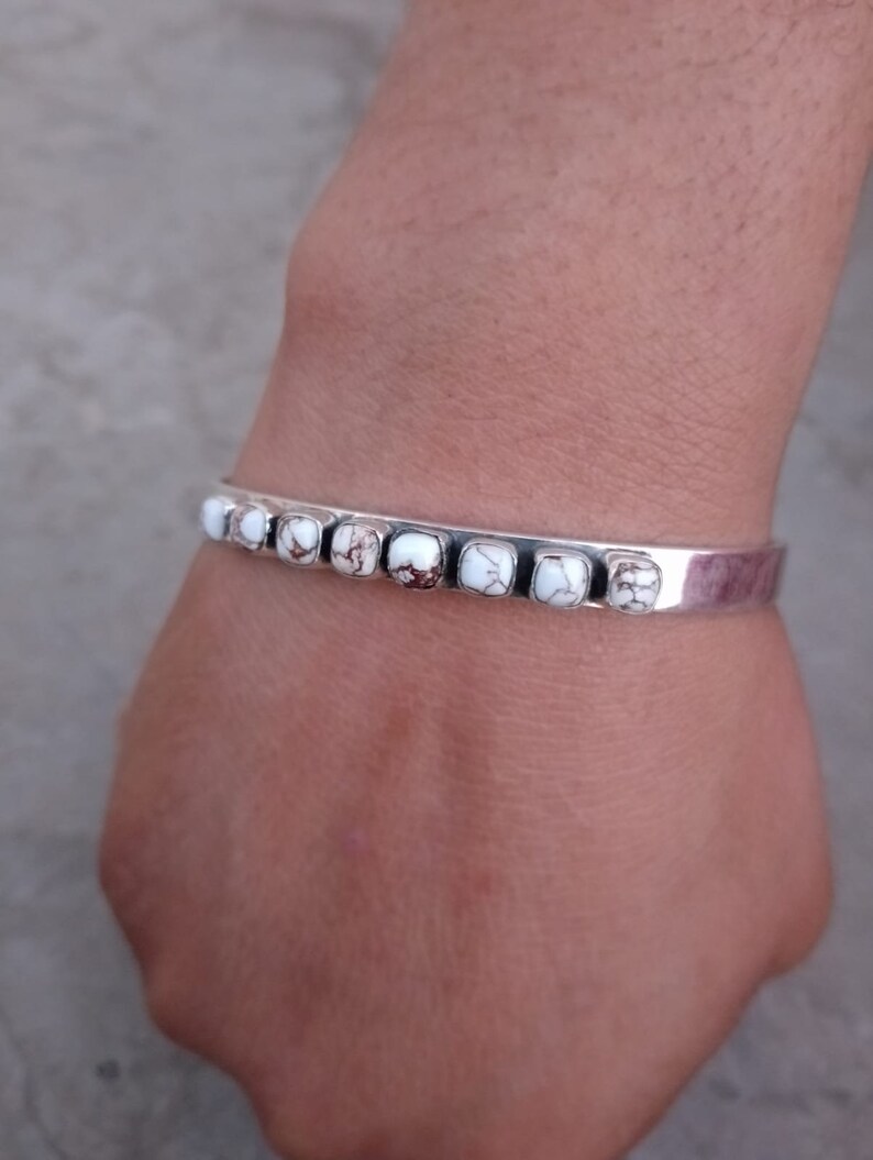 May include: A silver bracelet with white and brown stones. The bracelet is open and has a simple design.