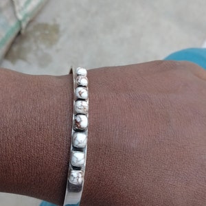May include: A silver bangle bracelet with white and brown marbled stones.