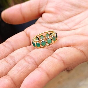 May include: A gold-toned ring featuring a series of small, round, smooth green cabochon stones set in a continuous row. The band has a twisted rope-like texture along the top and bottom edges, framing the circular green gemstones securely.