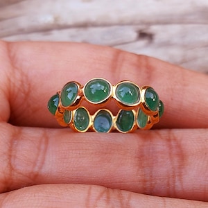 May include: A gold ring with a band of green gemstones. The ring is set with multiple oval-shaped stones.