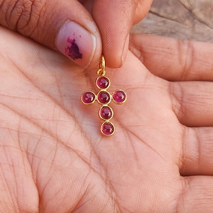 Peut inclure: Pendentif en forme de croix en or avec sept accents de pierres précieuses rouges.