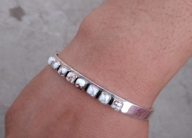 May include: A silver bangle bracelet with white and brown stones. The bracelet is open and has a simple design.