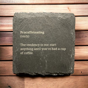 May include: A black slate coaster with the word "Procaffeinating" defined as "The tendency to not start anything until you've had a cup of coffee."