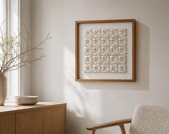 May include: A square wall art piece featuring a grid of twenty-five off-white, three-dimensional geometric tiles arranged in a five-by-five pattern, encased within a simple, light-toned wooden frame with a white mat border.