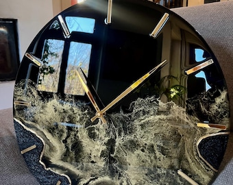 Peut inclure: Horloge en résine noire et dorée avec un design abstrait unique. Le cadran de l'horloge a des accents dorés et un fond noir avec des tourbillons dorés.