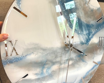 May include: A white and blue resin clock with Roman numeral markings and silver hands. The clock face has a marbled design with blue and white swirls.