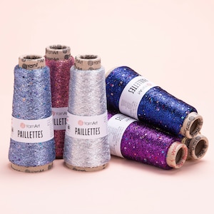 May include: Five spools of sparkly yarn with sequins. The yarn is in shades of blue, silver, pink, and purple. The spools are labeled "YarnArt Paillettes".