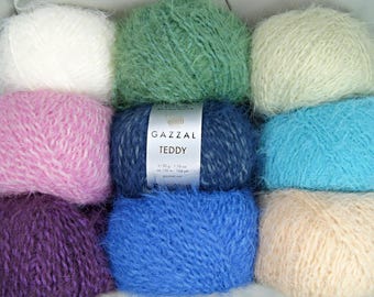May include: Assortment of ten skeins of Gazzal Teddy yarn in various colors, including white, green, light green, pink, blue, turquoise, purple, and cream. The label reads "Gazzal Teddy 50 g - 130 m - 1.76 oz - 142 yd - Gazzal Yarn."