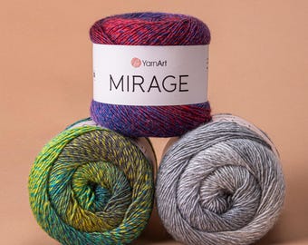May include: Three skeins of YarnArt Mirage yarn. The top skein is a mix of red and purple, with a white label that reads "MIRAGE". Below are two more skeins, one green and yellow, the other grey. The yarn is suitable for knitting and crochet.