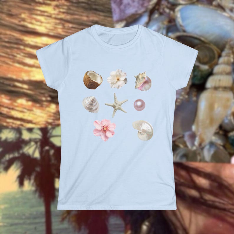May include: A light blue t-shirt featuring a collection of seashell and floral illustrations. The design includes a coconut, starfish, and various seashells in shades of white, pink, and beige. The shirt is a crew neck style.