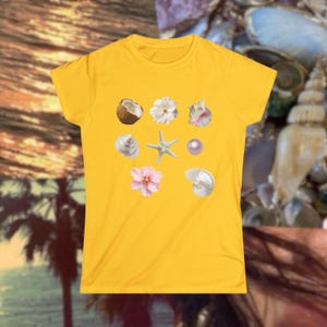 May include: A yellow t-shirt featuring a collection of seashell and floral graphics. The design includes a coconut, white and pink flowers, a starfish, a pearl, and various seashells. The shirt is a solid yellow color.