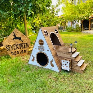 May include: Wooden rabbit house with a ramp and a platform. The house has a white roof with a cutout of a rabbit and the words "Seventeen Design".