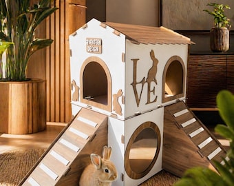 May include: A two-story wooden rabbit house with a white exterior and brown accents. The house features arched doorways, ramps, and the word "LOVE" cut out. A small brown rabbit sits in front of the house. The text "SEVENTEEN DESIGN" is visible.
