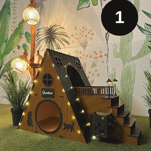 May include: A wooden A-frame pet house with a dark brown and black finish, featuring a circular entrance, two small round windows, and the word "Seventeen" on a plaque. It includes a side staircase, a balcony, and integrated warm string lights.