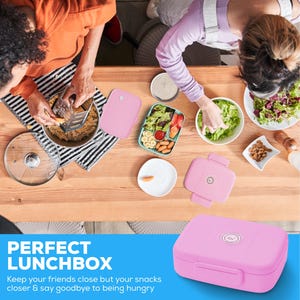May include: Pink lunchbox with a rounded rectangular shape and a secure latch. The lunchbox is on a wooden table with other lunch items, including a divided container with salad, fruit, and snacks. The text "PERFECT LUNCHBOX" is visible.