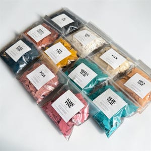 May include: A collection of colorful, handmade wax flakes in clear plastic bags. The bags are labeled with colors like "Dark Pink," "Blue Teal," and "Green Teal." The flakes are in various shades, including pink, yellow, and orange.