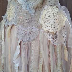 May include: A delicate, layered skirt made from crocheted doilies and sheer fabric. The skirt features a variety of textures and colours, including white, cream, and beige. The skirt is perfect for a bohemian or vintage-inspired look.