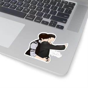 May include: A sticker featuring an illustration of two figures embracing. One figure is wearing a black vest over a light gray shirt, while the other is in a black jacket. The sticker is placed on a laptop.