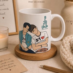 Peut inclure: Mug en céramique blanche avec une illustration de deux personnages et le texte turquoise "9 avec toi pour toujours". Le mug est posé sur un dessous de verre en bois. Une bougie allumée et une impression encadrée sont en arrière-plan.