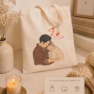 Peut inclure: Sac fourre-tout crème avec une illustration de deux personnages s'embrassant, avec du texte rouge et noir. Le sac a des poignées crème et la phrase "FOR EVERY BL HEART" en bas.
