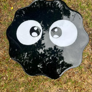May include: Black resin table top with a wavy edge and two large white eyes with black pupils. The table top is reminiscent of a cartoon character.
