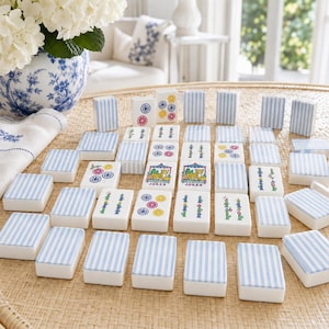 May include: A set of rectangular mahjong tiles featuring a white base with blue vertical stripes on the back. The front faces display various colorful illustrations, including floral patterns, bamboo stalks, and two tiles labeled Joker.