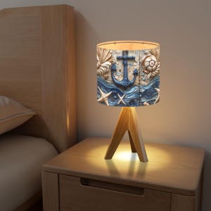 May include: A table lamp with a wooden base and a fabric lampshade featuring a blue anchor and seashells on a blue and white background.