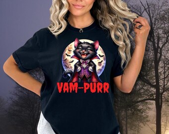 Może przedstawiać: Czarny t-shirt z kreskówkowym kotem przebranym za wampira z napisem "VAM-PURR" w kolorze czerwonym. Kot jest umieszczony na tle pełni księżyca z nietoperzami. Koszulka graficzna z motywem Halloween.