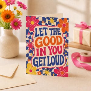May include: A greeting card featuring a blue and white checkered background with colorful flowers and star shapes. The text in the center reads, Let the good in you get loud, in bold orange, pink, and blue lettering against a cream-colored backdrop.