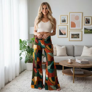 May include: A woman wearing a cream-colored crop top and patterned palazzo pants. The pants feature a colorful geometric design in shades of orange, green, and yellow. The pants have a flared leg and a drawstring detail at the waist.