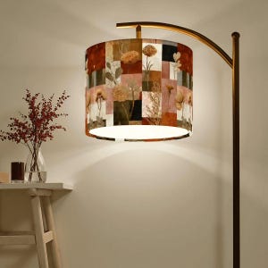 May include: A floor lamp with a patterned lampshade. The lampshade features a patchwork design with floral and botanical motifs in shades of brown, beige, and red. The lamp has a curved, bronze-colored metal arm and a dark brown pole.