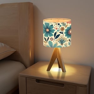 May include: A bedside table lamp with a wooden tripod base and a white lampshade with a floral pattern in shades of blue, green, and pink.