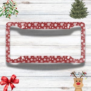 May include: Red license plate frame with a white snowflake pattern. The frame is made of metal and has holes for mounting.