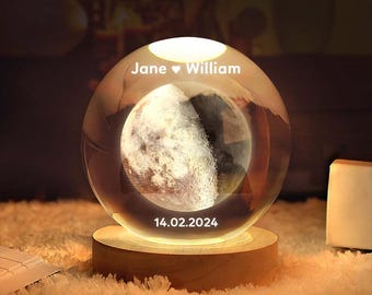 May include: A clear glass moon lamp with a wooden base. The lamp features a 3D moon design and is illuminated from within. The lamp is engraved with the names "Jane ♥ William" and the date "14.02.2024".