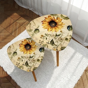 May include: Two small, uniquely shaped side tables. Each table features a large sunflower design with yellow petals and a dark center. The tables have light brown wooden legs and are set on a white rug.