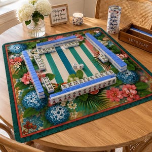 May include: A Mahjong game set on a round wooden table. The game board features a green and white striped design with blue and white tiles. The board is surrounded by floral patterns with blue and pink flowers. A wooden box with the words "LET'S PLAY" is visible.