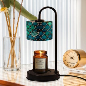 May include: A black metal lamp with a teal and green patterned lampshade. The lamp has a round base and a candle warmer on top. A brown glass candle is sitting on the warmer. A gold clock with black hands and the text "SOTTILE MA GIAIE" is on the table.