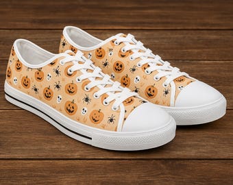 May include: A pair of canvas sneakers with a Halloween-themed pattern. The shoes feature a light orange background with repeating images of jack-o'-lanterns, spiders, and skulls. The sneakers have white laces, toe caps, and soles, with a black stripe.