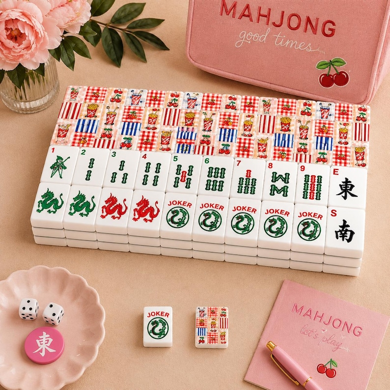 May include: A set of mahjong tiles featuring white tiles with green and red symbols, including dragons and jokers, alongside tiles with red and blue checkered patterns. Includes two white dice, a pink storage case, and a pink notebook with text.