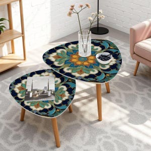 May include: Two matching, triangular side tables with a detailed floral pattern in shades of blue, teal, gold, and cream. The tables have light wood legs and are arranged on a patterned rug. One table has a vase with flowers and a bowl of berries.
