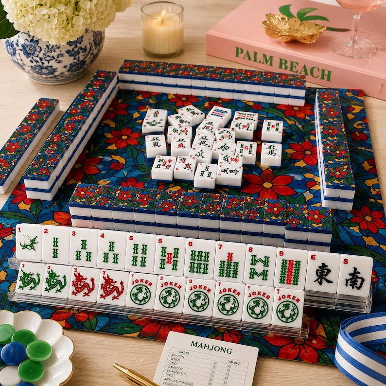 Puede incluir: Un juego de Mahjong completo con fichas blancas con s&iacute;mbolos verdes y rojos, presentado sobre un tapete con estampado floral. El juego incluye estantes, dados y una hoja de puntuaci&oacute;n.