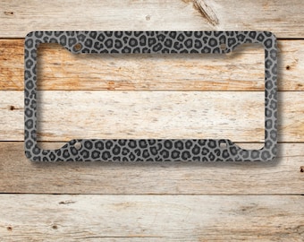 May include: A black and gray leopard print license plate frame. The frame is made of metal and has a sleek, modern design.