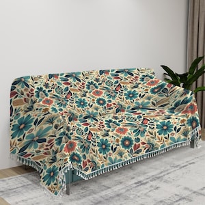 May include: A floral patterned throw blanket with a fringe border in shades of blue, red, and cream. The blanket is draped over a couch.